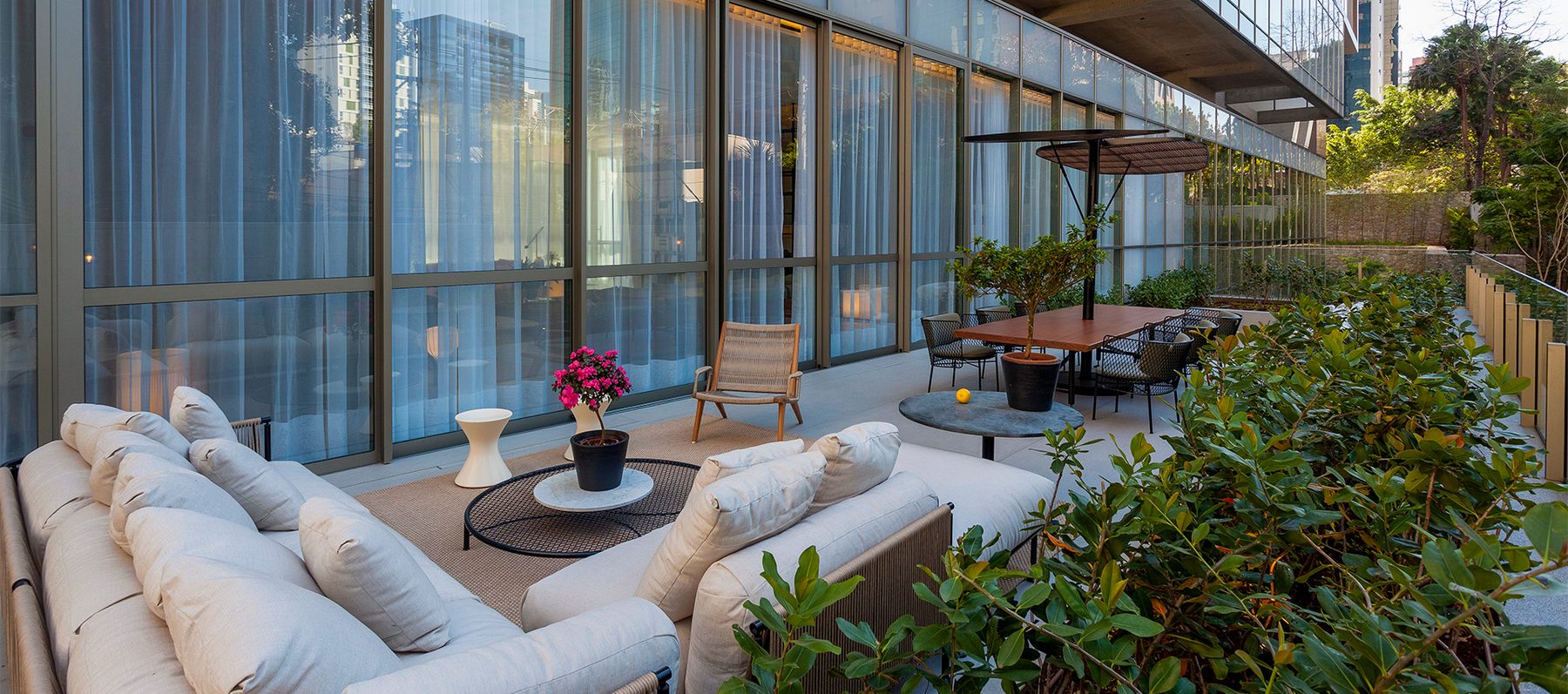 Lounge externo do Casa Brasileira Itaim, com sofás, paisagismo nativo e fachada envidraçada