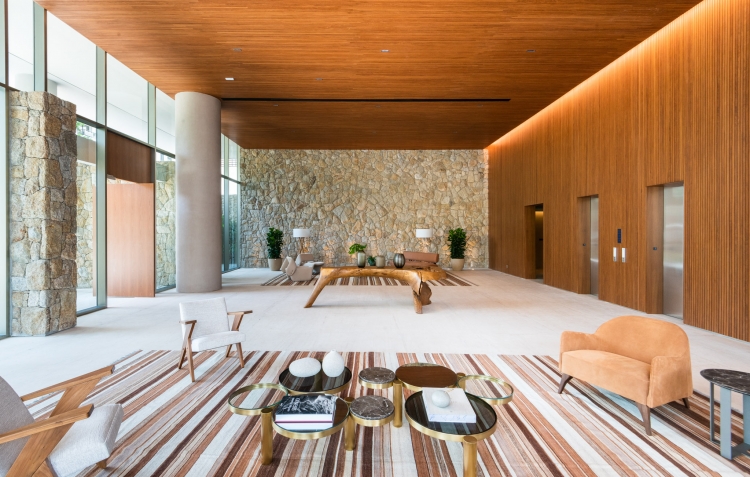Estar do lobby do Casa Leopoldo, com poltronas, mesa de madeira maciça e vidros do piso ao teto, no Itaim Bibi