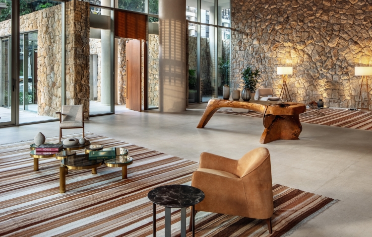 Área de convívio do Casa Leopoldo integrada aos jardins, com paredes de pedra e mobiliário de design, no Itaim Bibi